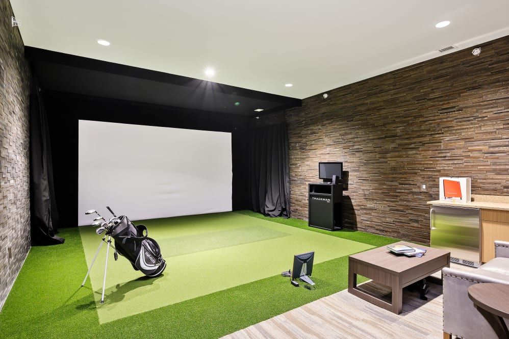An indoor golf simulator with artificial turf and a projector screen, featuring a golf bag.