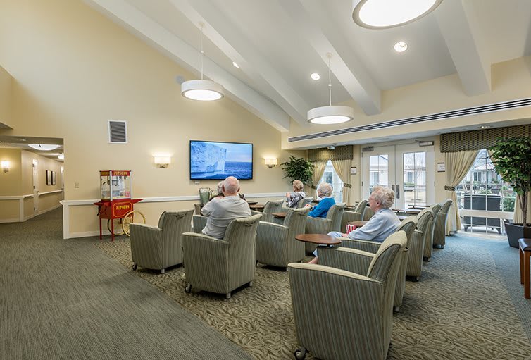A group of seniors sitting in a community room watching television and socializing.