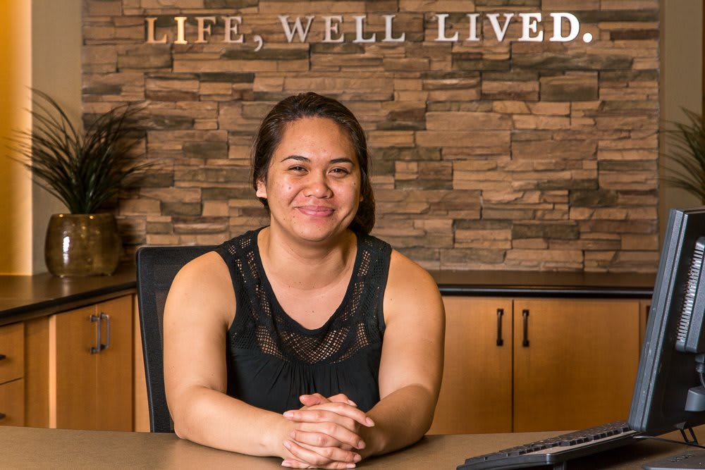 A woman smiling while sitting at a desk in an office setting.