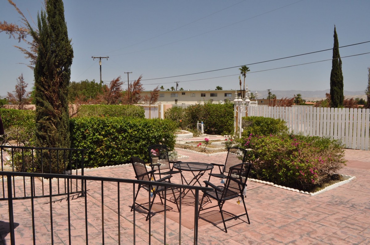A patio with metal chairs and a table, surrounded by a garden and bushes.
