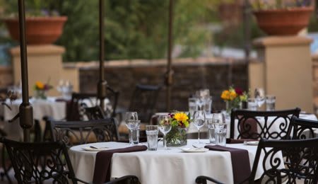 An elegantly set outdoor restaurant table adorned with flowers and glassware.