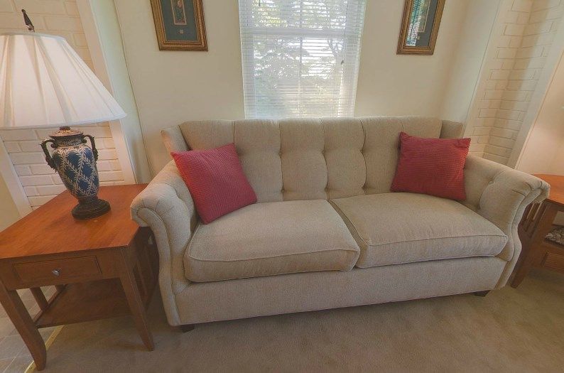 A cozy living room featuring a beige sofa with red pillows, next to a wooden side table and lamp.