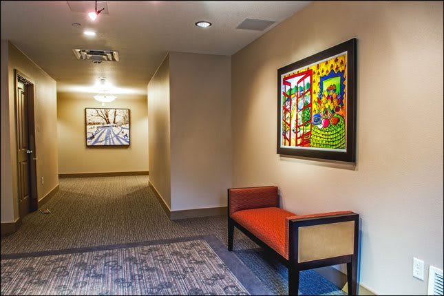 A modern hallway features colorful artwork and a red cushioned bench.