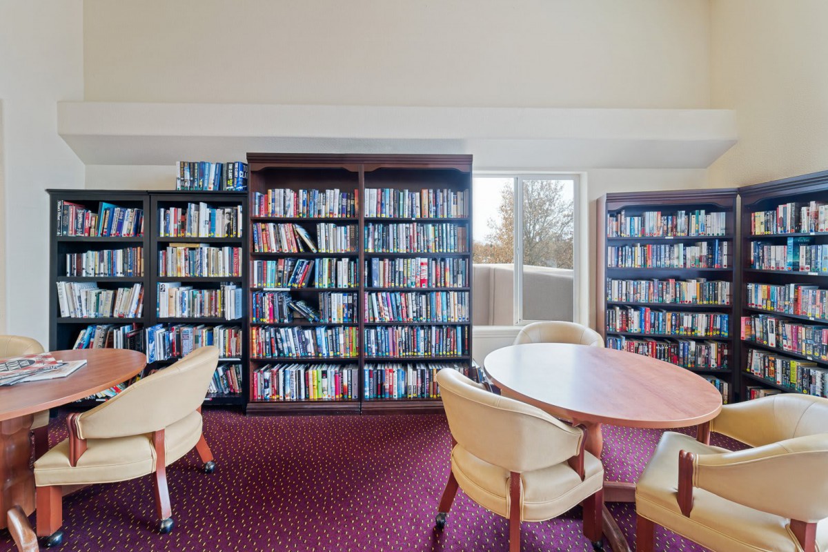 A cozy library reading area with bookshelves, tables, and chairs.