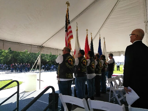 A group of veterans stands in formation during a flag presentation ceremony under a tent.