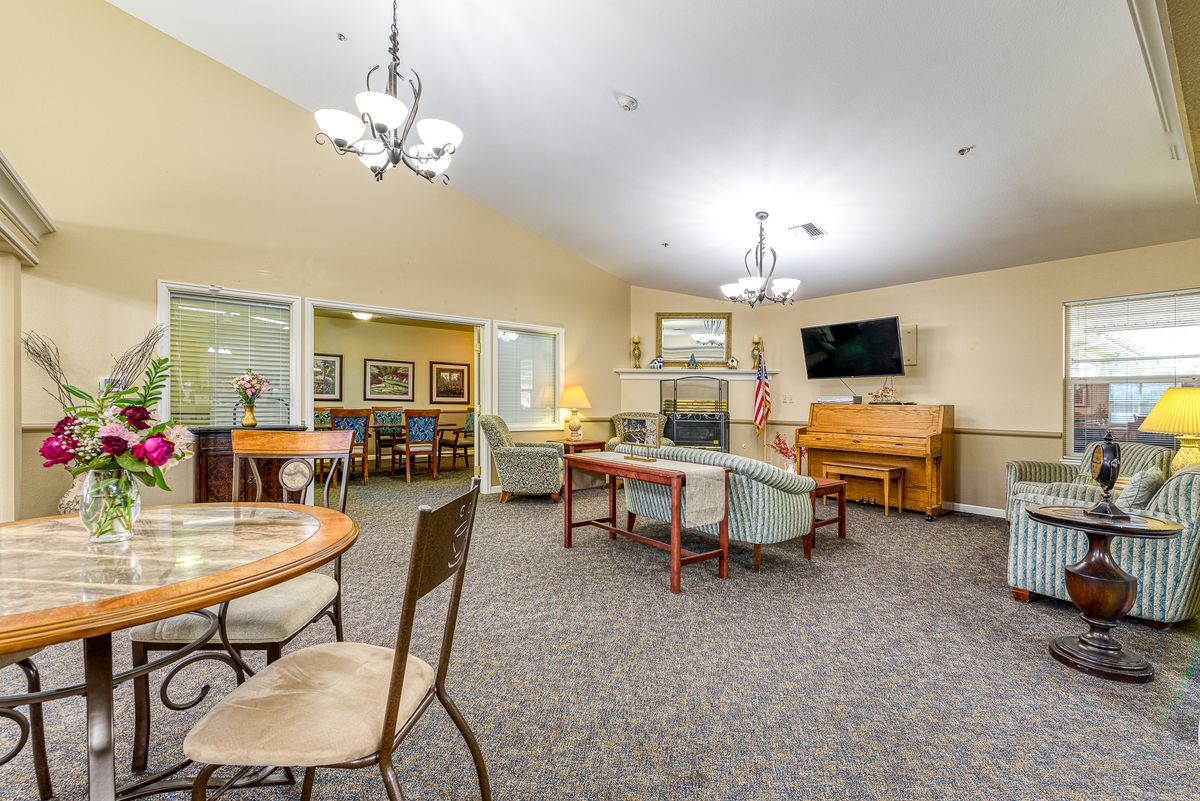 A spacious living room featuring comfortable seating, a TV, and a piano, illuminated by elegant chandeliers.