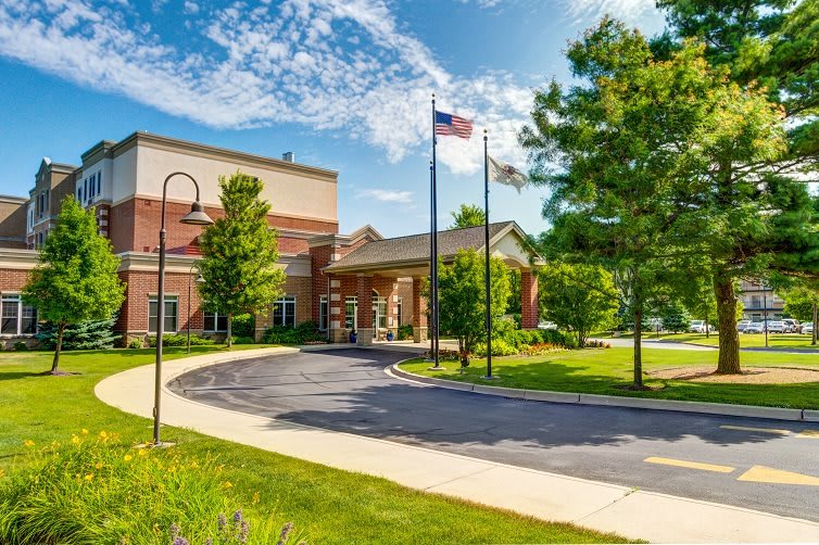 A sunny day at a building entrance with flags and lush trees along a curved driveway.