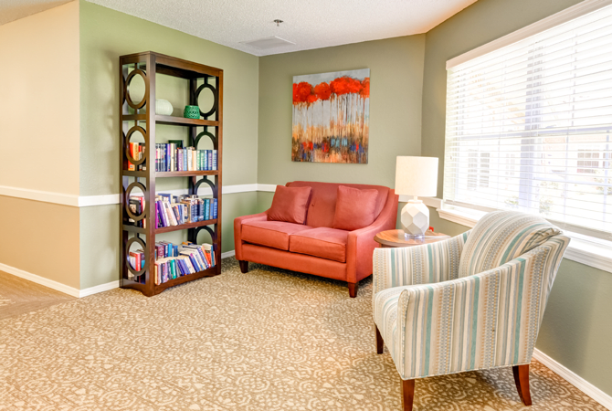 A cozy living room with a red couch, striped armchair, and a bookshelf filled with books and decorative items.