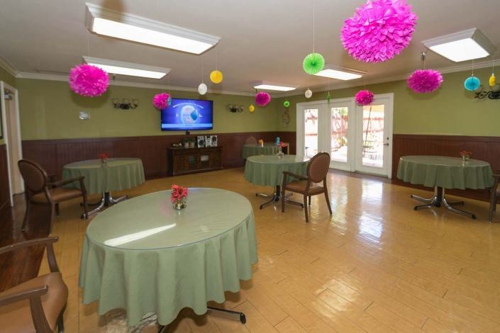 A brightly decorated dining room featuring tables with green tablecloths and colorful pompoms hanging from the ceiling.