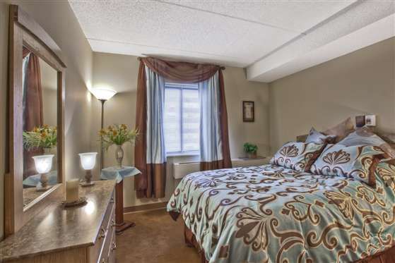 A cozy bedroom with a patterned bedspread, standing lamp, and natural light from a window with curtains.