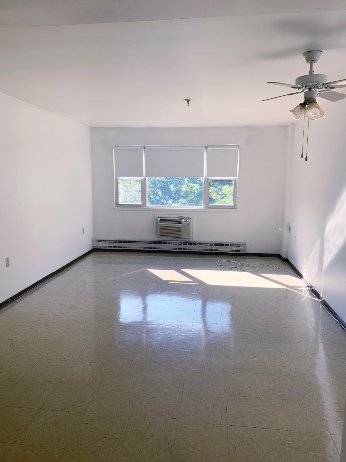 A minimalist empty room with plenty of natural light coming through a window, featuring a ceiling fan.