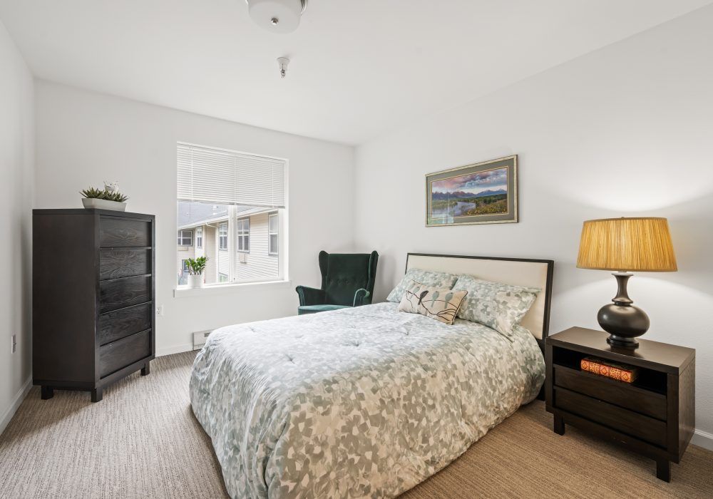 A cozy bedroom with a patterned bedspread, dark wooden furniture, and a painting above the bed.