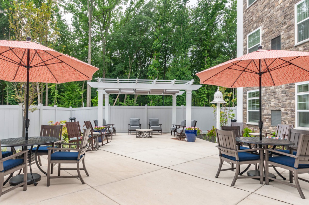 A cozy outdoor patio with seating arrangements under large umbrellas, surrounded by trees and a pergola.