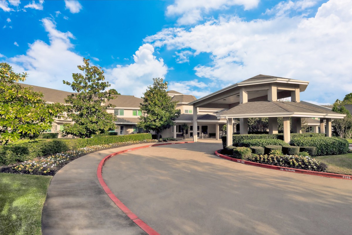 A well-maintained residential building with a circular driveway and landscaped surroundings under a partly cloudy sky.