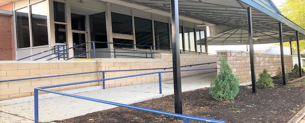 A building entrance featuring a series of ramps with blue handrails.