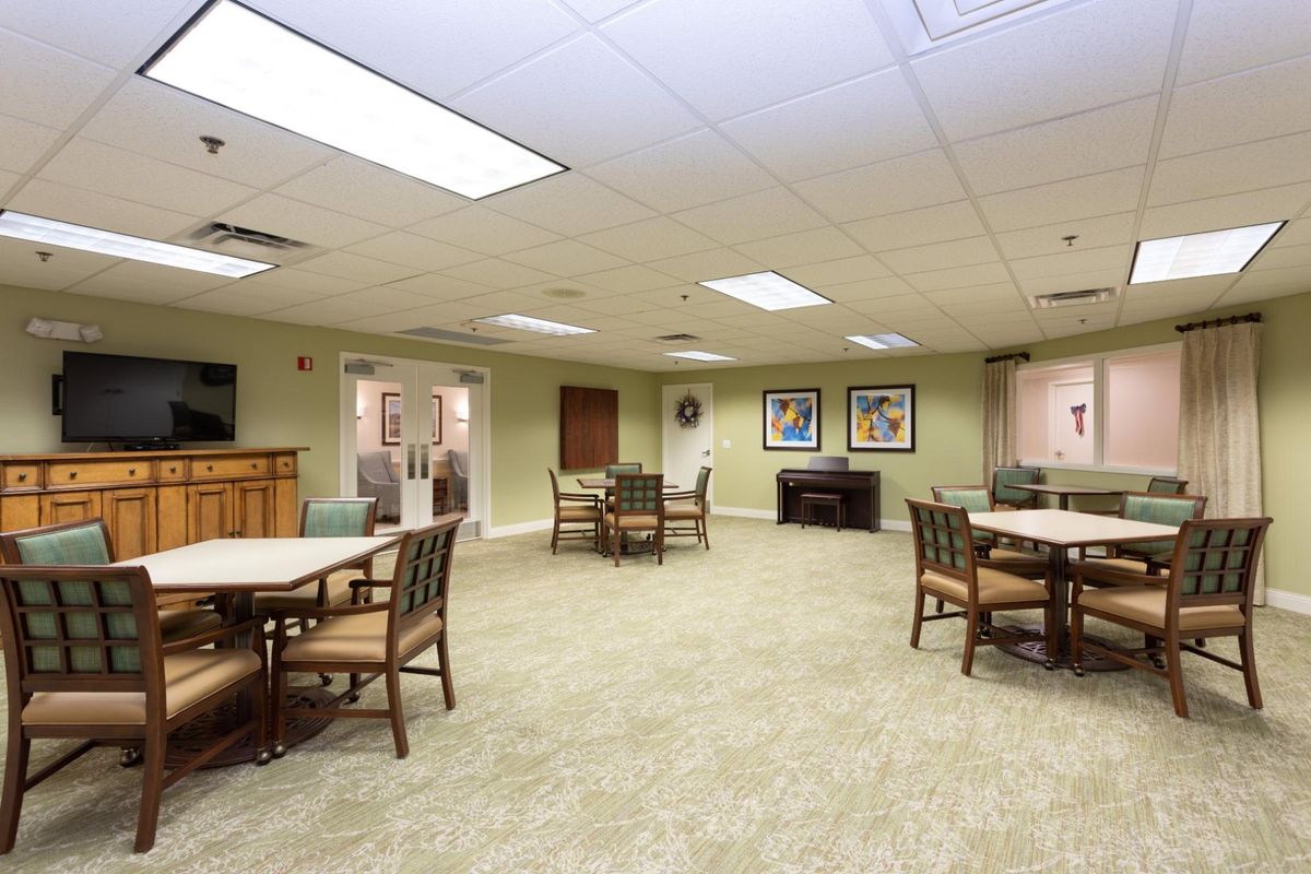 A spacious room with multiple tables and chairs, carpeted flooring, and artwork on the walls.