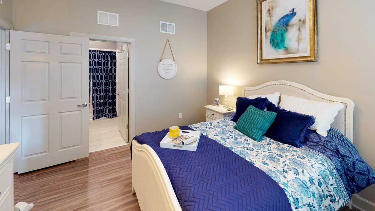 A cozy bedroom setup featuring a neatly made bed with blue and patterned bedding, a bedside lamp, and wall art.