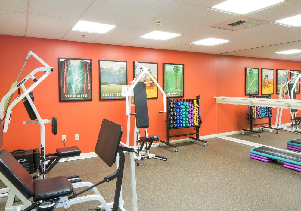 A bright gym room featuring various fitness equipment against orange walls.