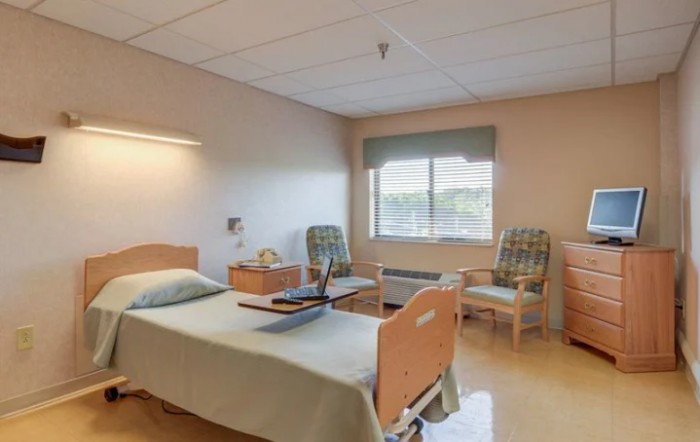 A clean and organized hospital room with a bed, chairs, and a window.