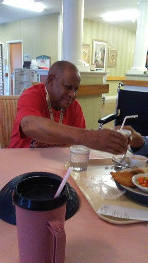 An elderly man enjoying a meal at a restaurant, sharing a drink with someone.