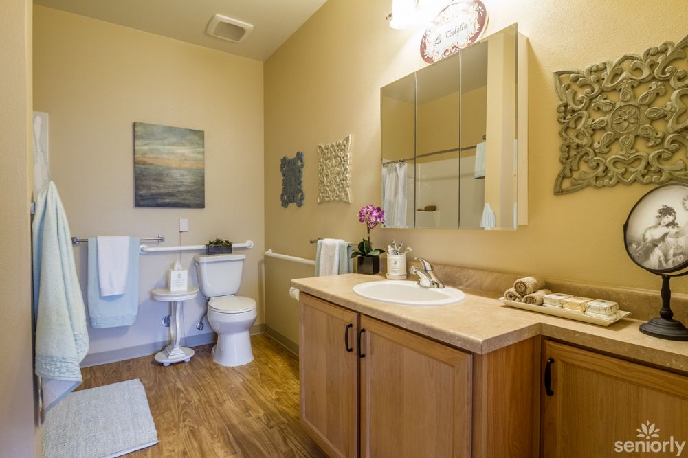 A clean and well-organized bathroom with wooden cabinets, a mirror, and wall decorations.