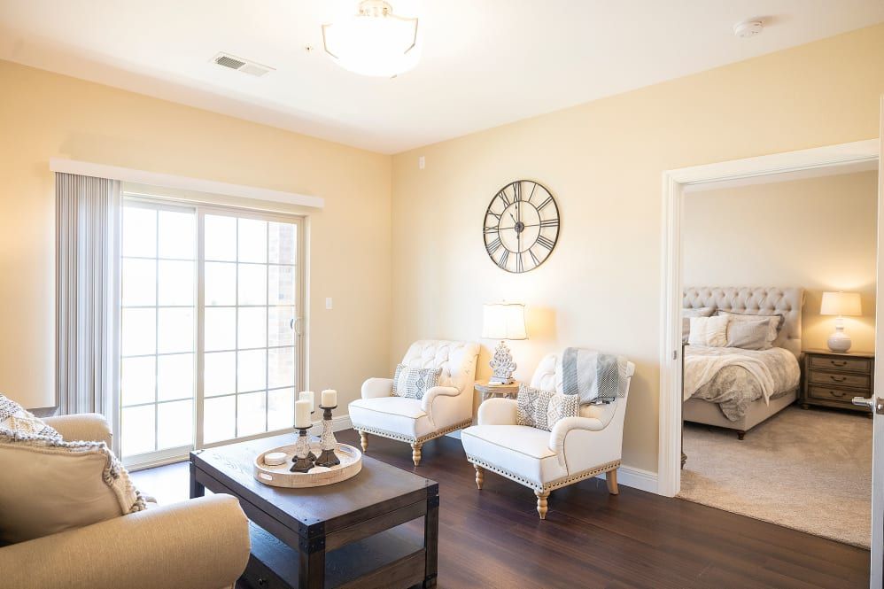 A bright living room with two armchairs, a coffee table, and a wall clock.