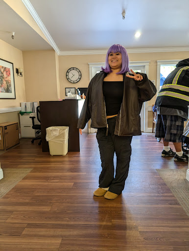 A person with purple hair in a casual outfit strikes a playful pose indoors.