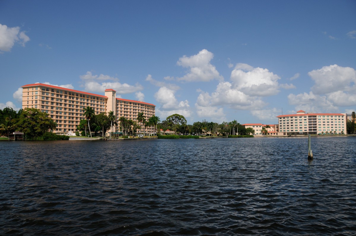 A scenic view of buildings by the lakeside under a clear blue sky with fluffy clouds.