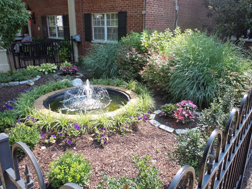 A serene garden featuring a central fountain surrounded by lush plants and colorful flowers.