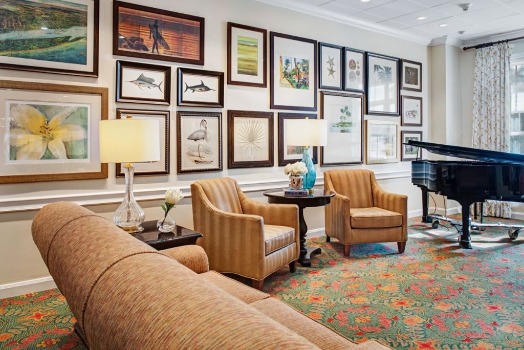 A cozy living room with a gallery wall of framed art, featuring comfortable seating and a grand piano.