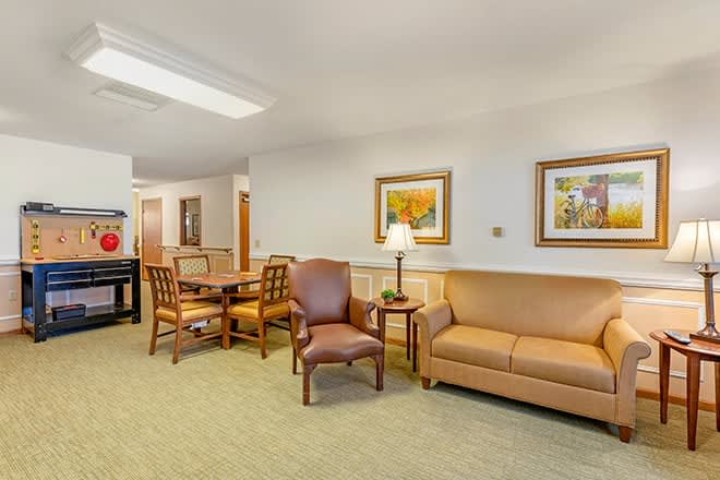 A cozy living area with a sofa, chairs, and a dining table, decorated with artwork and a lamp.
