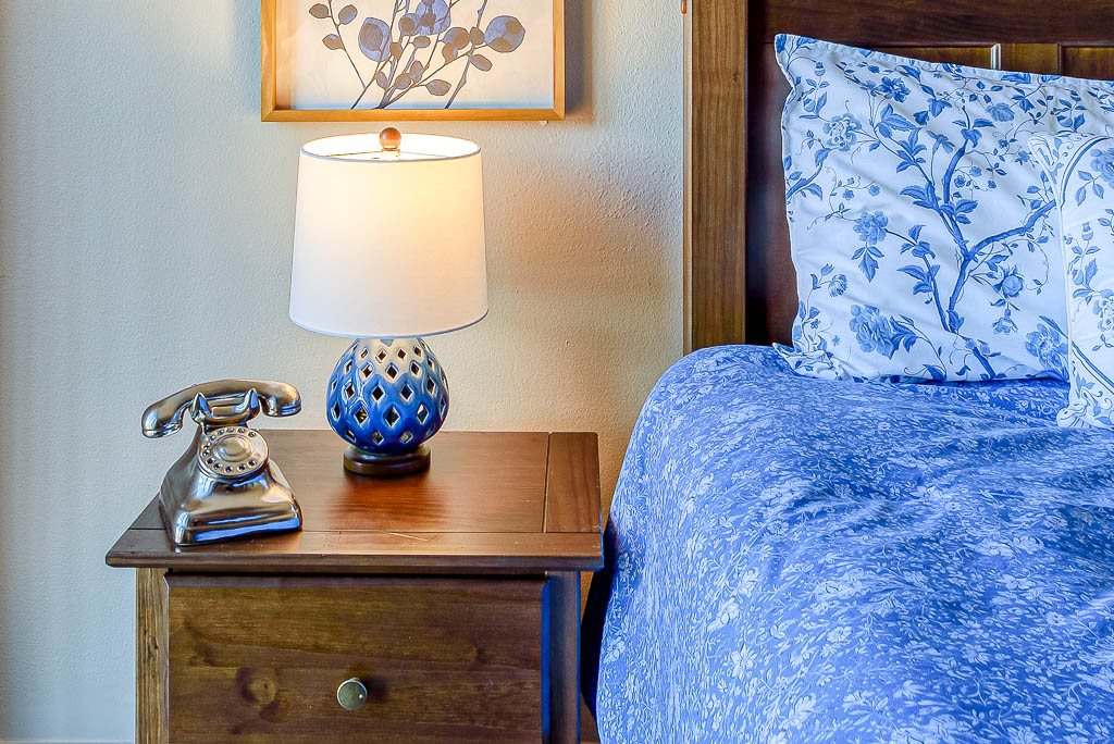 A cozy bedroom scene featuring a wooden nightstand with a decorative lamp and floral bedding.
