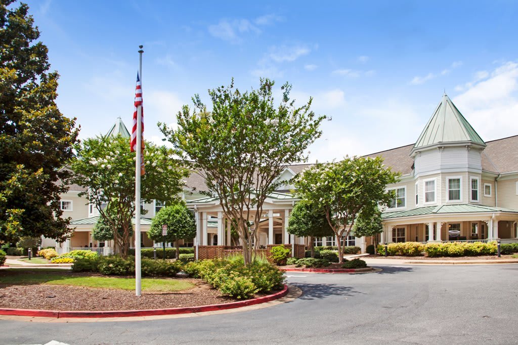 A large building with a flagpole surrounded by landscaped trees and a parking area.