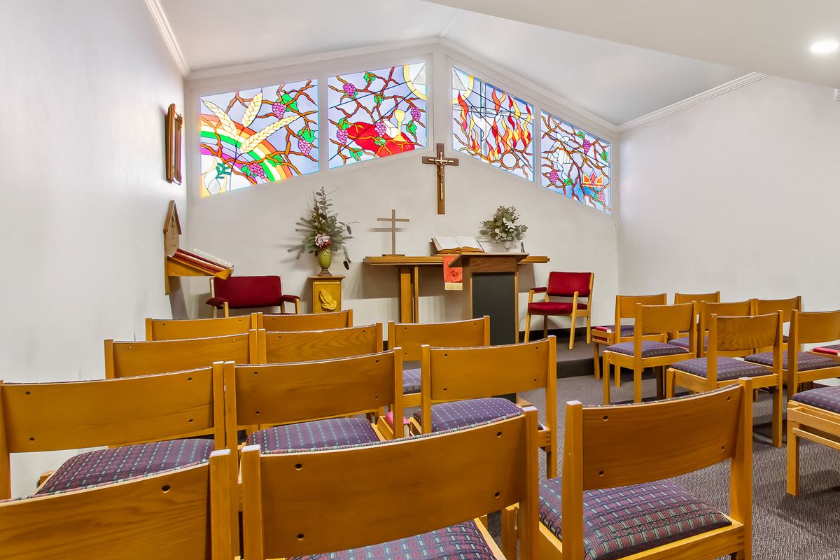 Interior view of a small chapel with stained glass windows, wooden pews, and an altar.