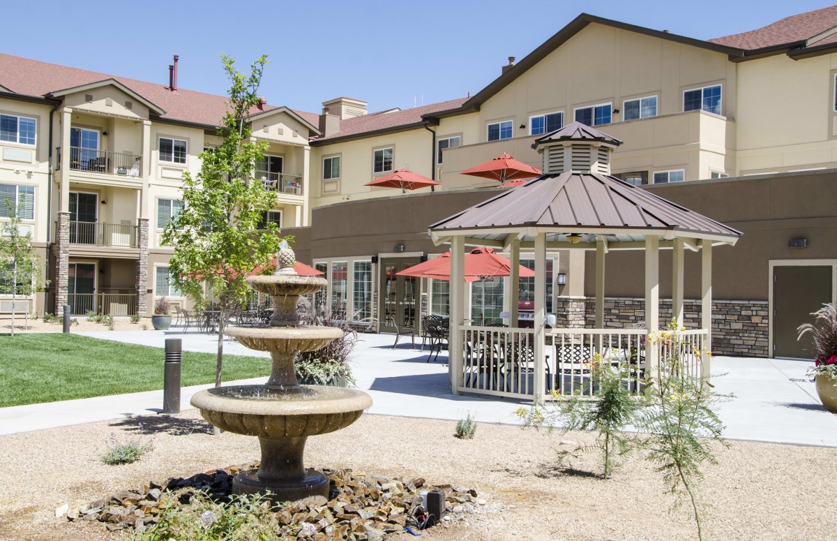 A sunny outdoor area with a fountain, gazebo, and seating with umbrellas.