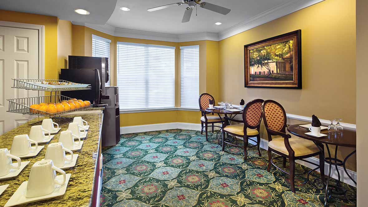 A cozy dining area with a round table and chairs, featuring a patterned carpet and large windows.