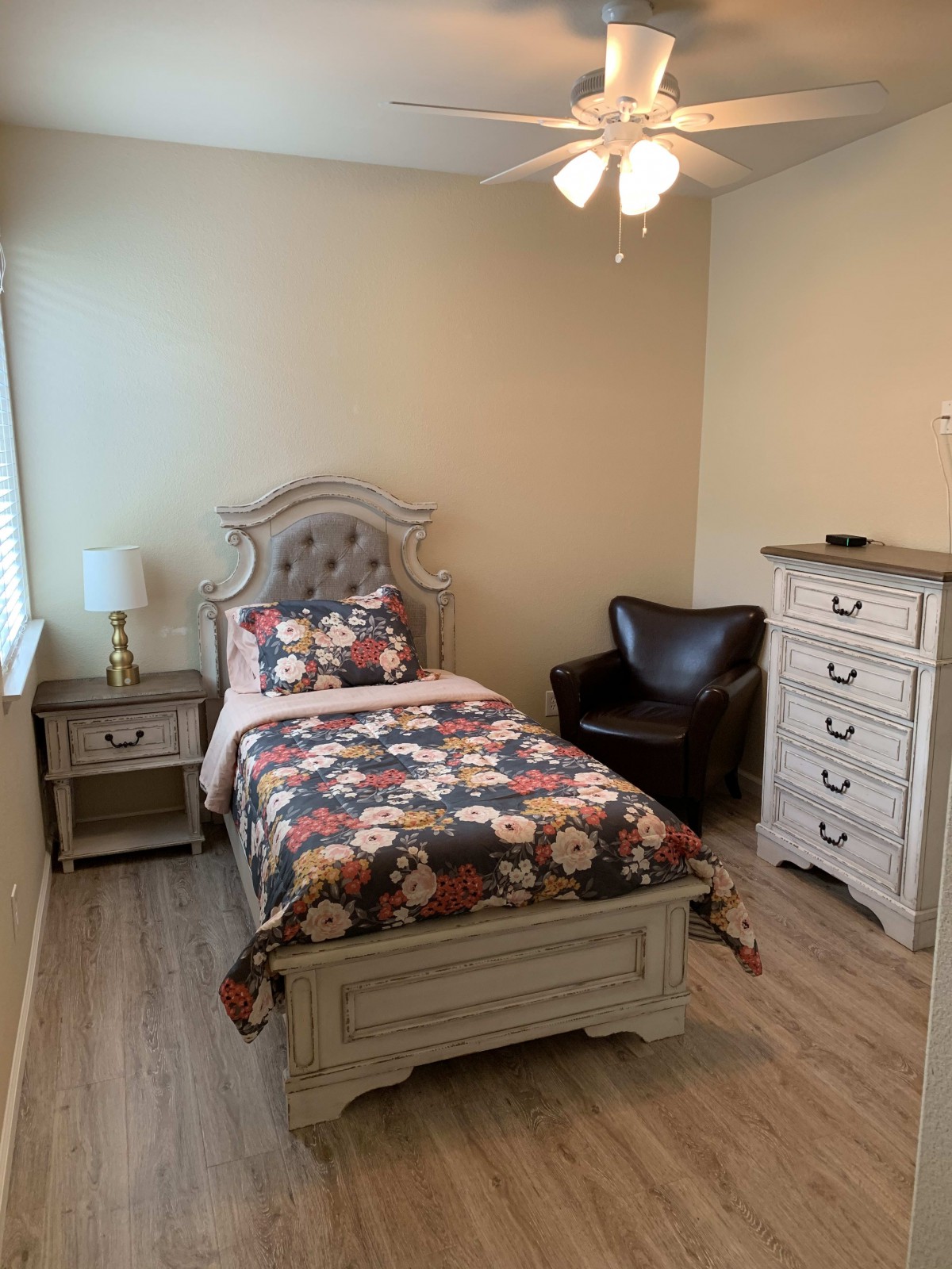 A cozy bedroom with a single floral-patterned bed, wooden furniture, and an armchair.