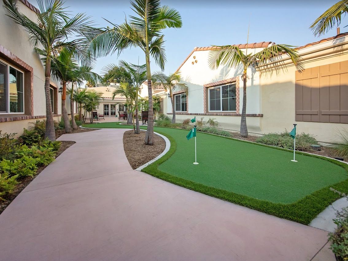 A serene outdoor area featuring a putting green, surrounded by palm trees and a well-maintained pathway.