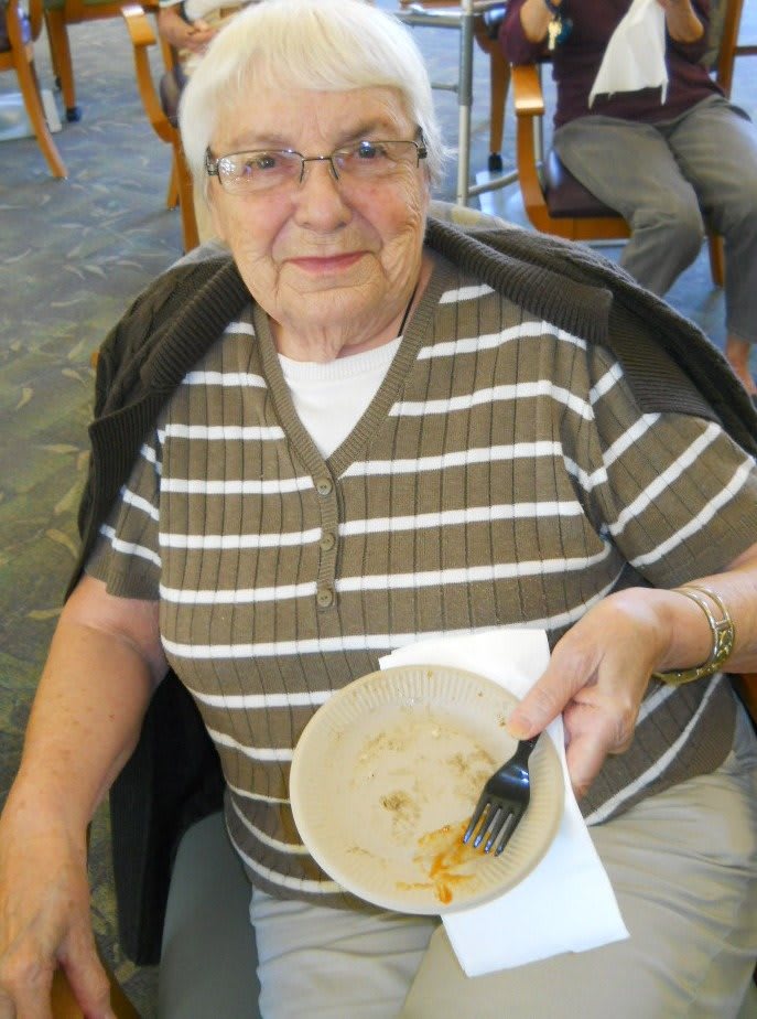 An elderly woman sitting and holding an empty plate after a meal.