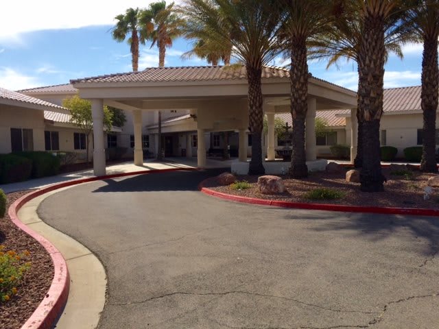 A building entrance with a driveway and palm trees in the foreground.
