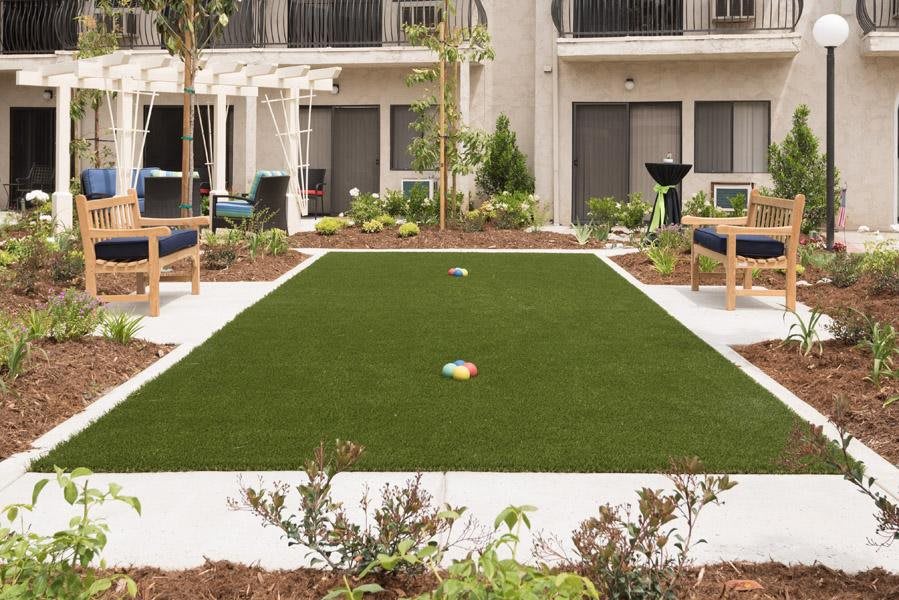 A modern courtyard featuring artificial grass, surrounded by benches and stylish landscaping.