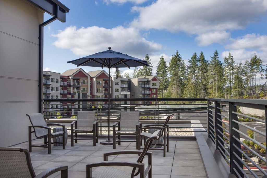 A scenic patio area with chairs and an umbrella overlooking nearby buildings and trees under a partly cloudy sky.