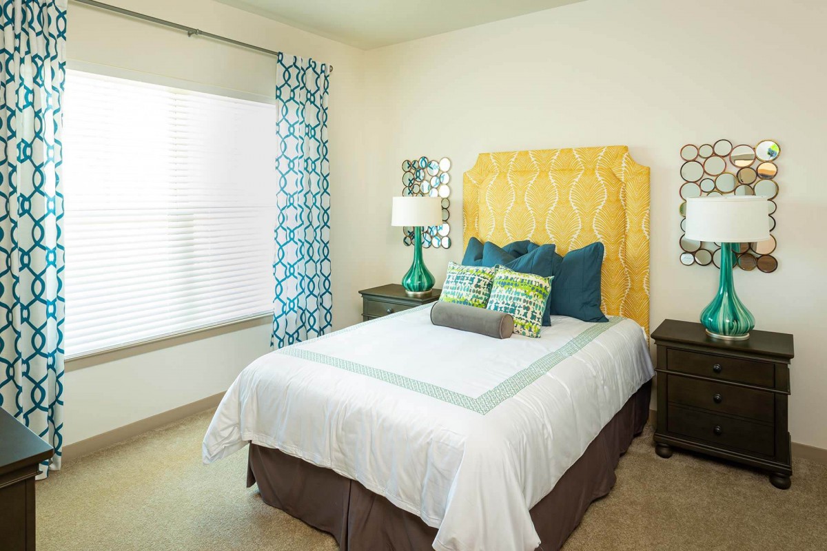 A cozy, colorful bedroom with a neatly made bed, patterned curtains, and decorative pillows.