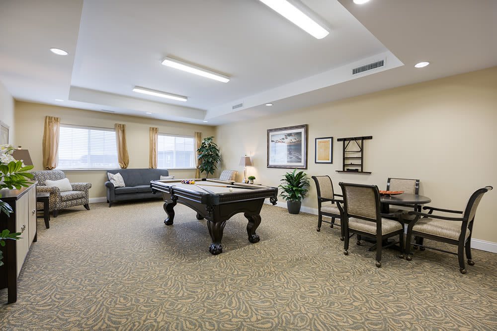 A spacious recreation room featuring a pool table, comfortable seating, and indoor plants.