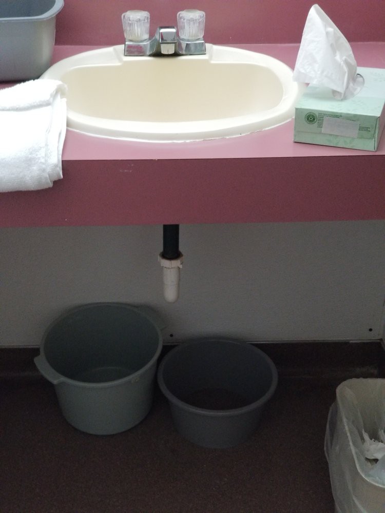 Bathroom setup with a sink, towels, and buckets underneath the counter.