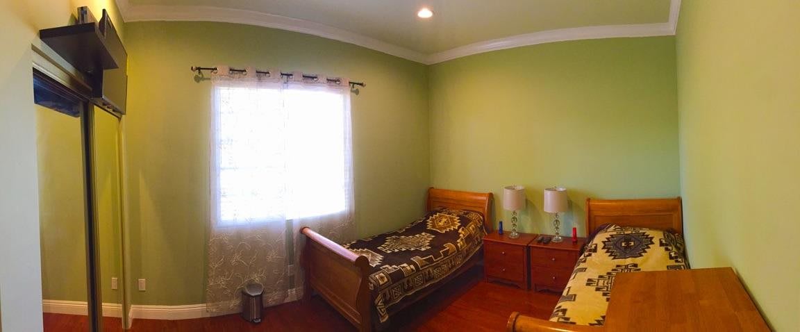 A cozy bedroom with green walls, featuring a single wooden bed and warm lighting.