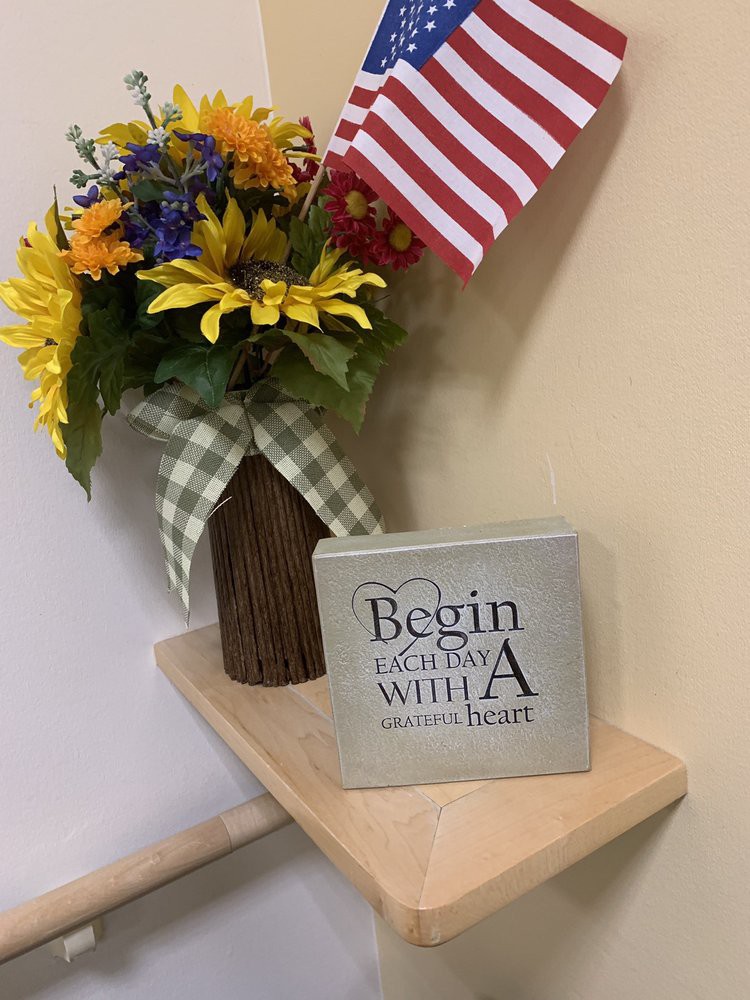 A decorative arrangement featuring a vase of colorful flowers, an American flag, and a sign with an inspirational quote on a small shelf.