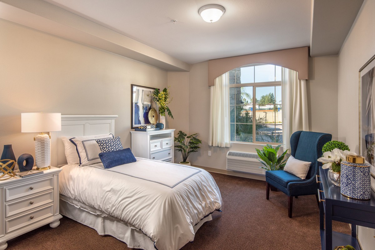 A well-lit bedroom with a single bed, armchair, and large window.