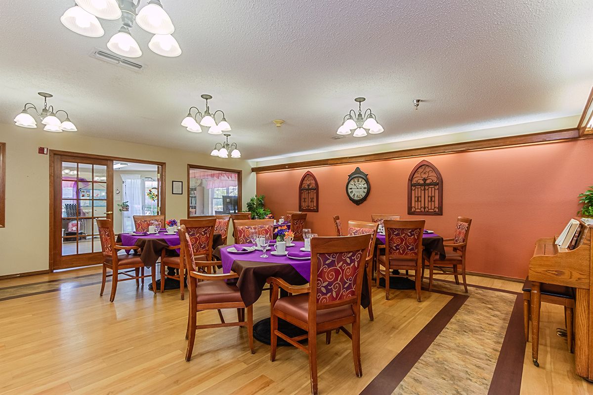 A warmly lit dining room with neatly arranged tables covered in purple tablecloths.