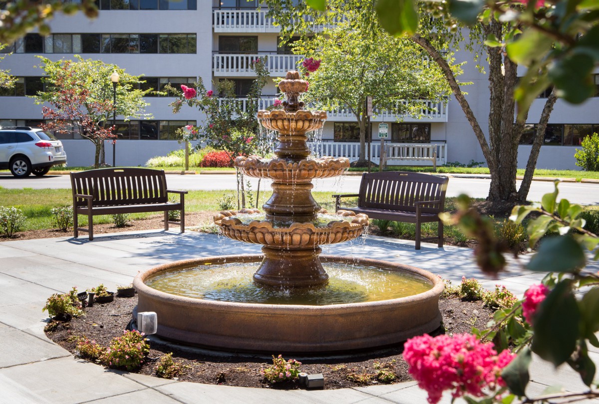 A picturesque outdoor garden with a central fountain surrounded by benches and vibrant flowers.